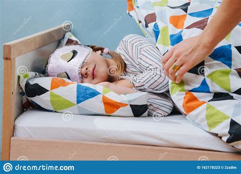 Moeder Neemt Haar Dochter In Bed Op Meisje Met Slaapmasker Stock