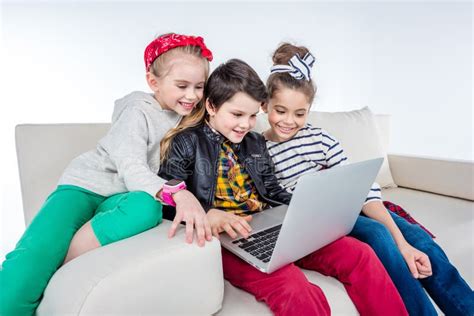 Smiling Children Using Laptop While Sitting On Sofa Stock Photo Image