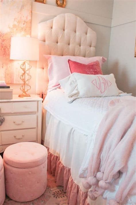 A White Bed Sitting Next To A Pink Ottoman And Table With A Lamp On Top Of It