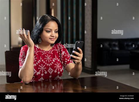 A Young Indian Woman Sitting In Her Living Room Holding Her Mobile