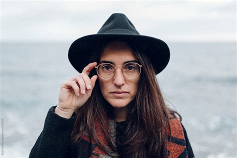 woman with a black hat scarf and glasses looking at the camera near the sea on a winter day