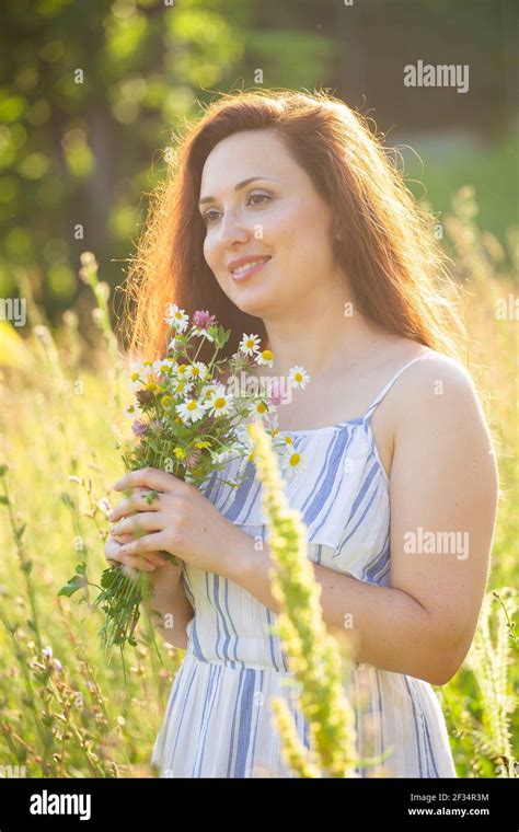 Close Up Portrait Of Beautiful Young Woman Sniffing Bouquet Of Beautiful Wildflowers On Sunny