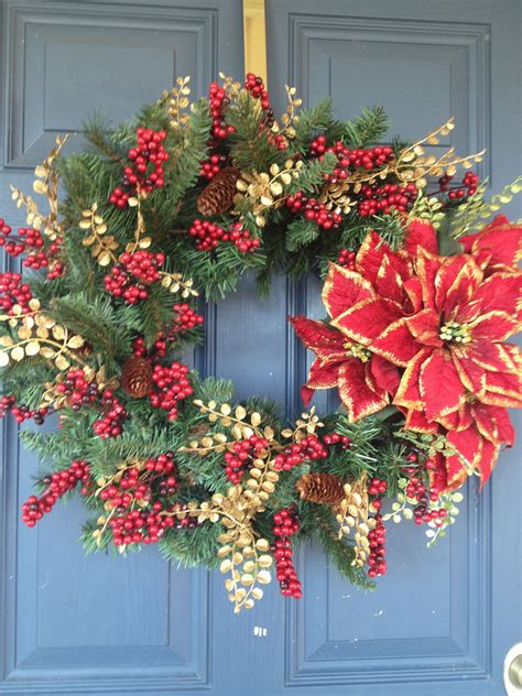 A Christmas Wreath With Poinsettis And Pine Cones On A Blue Front Door
