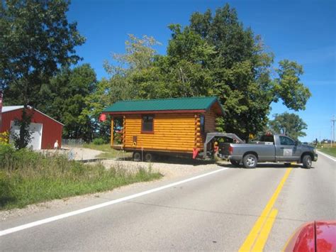 A Truck Pulling A Log Cabin On The Side Of A Road