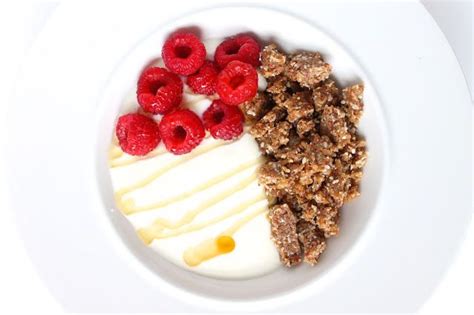 A White Plate Topped With Granola Yogurt And Raspberries