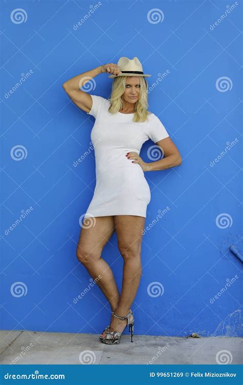 Mujer Rubia Madura Atractiva Que Presenta En El Vestido Blanco En La Pared Azul Imagen De