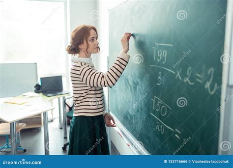 Beautiful Teacher Writing The Task On The Blackboard Stock Photo