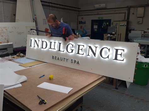 A Man Working On A Sign That Says Indulgence Beauty Spa In Front Of It
