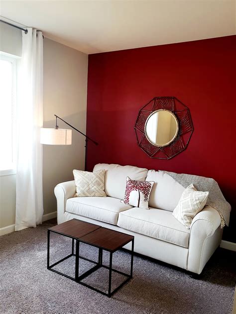 A Living Room With A White Couch And Red Wall In The Corner Along With