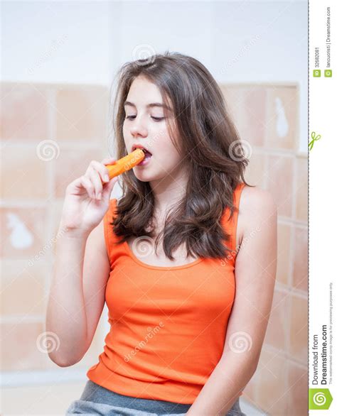 Девочка подросток в оранжевой футболке есть морковь Стоковое Изображение изображение
