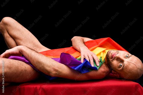 Naked Adult Gay Man With Shaved Head Lying With Lgbt Flag Isolated On