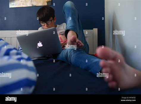 A Teenage Boy Age 14 Lays On His Bed With A Mac Book Air Laptop Doing