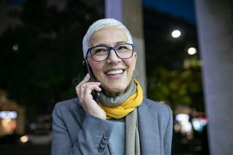 Smiling Mature Senior Woman With Short Gray Hair And Eyeglasses Use Phone On Street Night Scene