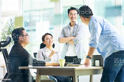 Group Of Young Asian Business Executives Talking In Office Stock Photo