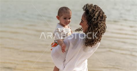 صورة مقربة لأم عربية خليجية سعودية تحمل إبنتها بحب وحنان، أم تلعب مع إبنتها بإيماءات وجه ويدين