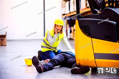 An Accident In A Warehouse Woman With Smartphone And Her Colleague Lying On The Floor Next To A