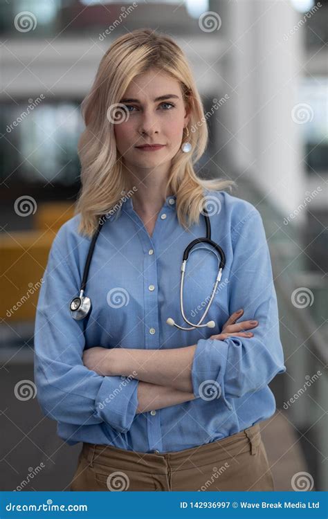 Blonde Female Doctor With Arms Crossed Looking At Camera In Clinic
